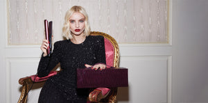 Woman in a black dress holding a purple clutch and box in an elegant room.