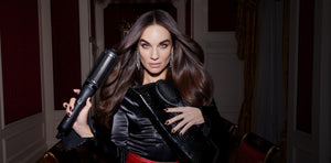 Woman holding a hair dryer and a black handbag in an indoor setting